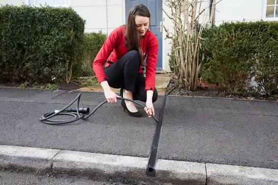 Person feeding an EV charging cable into a self-closing cross-pavement channel outside a house