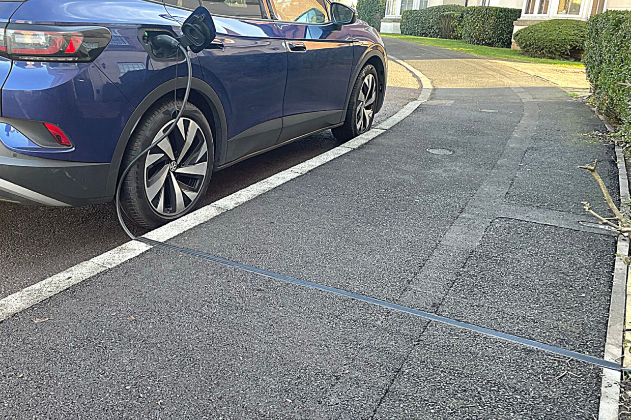 EV charging cable running through a channel set flush into the pavement to a blue electric car parked at the kerb